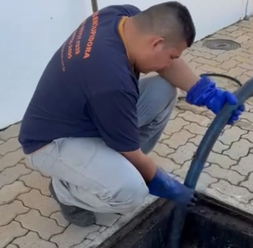Profissional uniformizado da Desentupidora Itape desentupindo sistema de esgoto com equipamento manual